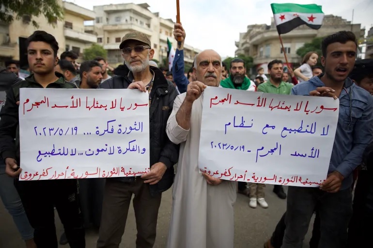 Para pengunjuk rasa memegang spanduk bertuliskan: 'Suriah tidak diwakili oleh penjahat al-Assad' dan 'Tidak untuk normalisasi dengan rezim' di Idlib yang dikuasai pemberontak. Foto: Ali Haj Suleiman/Al Jazeera.